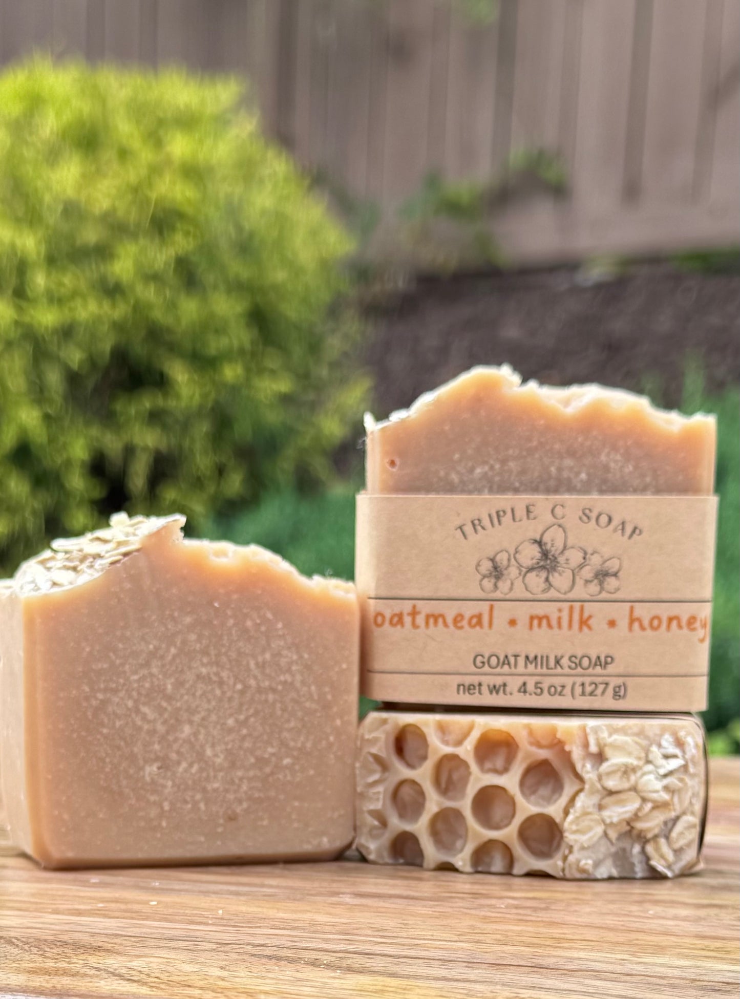 Three bars of soap labeled 'Triple C Soap' oatmeal milk honey on a wooden surface outdoors.