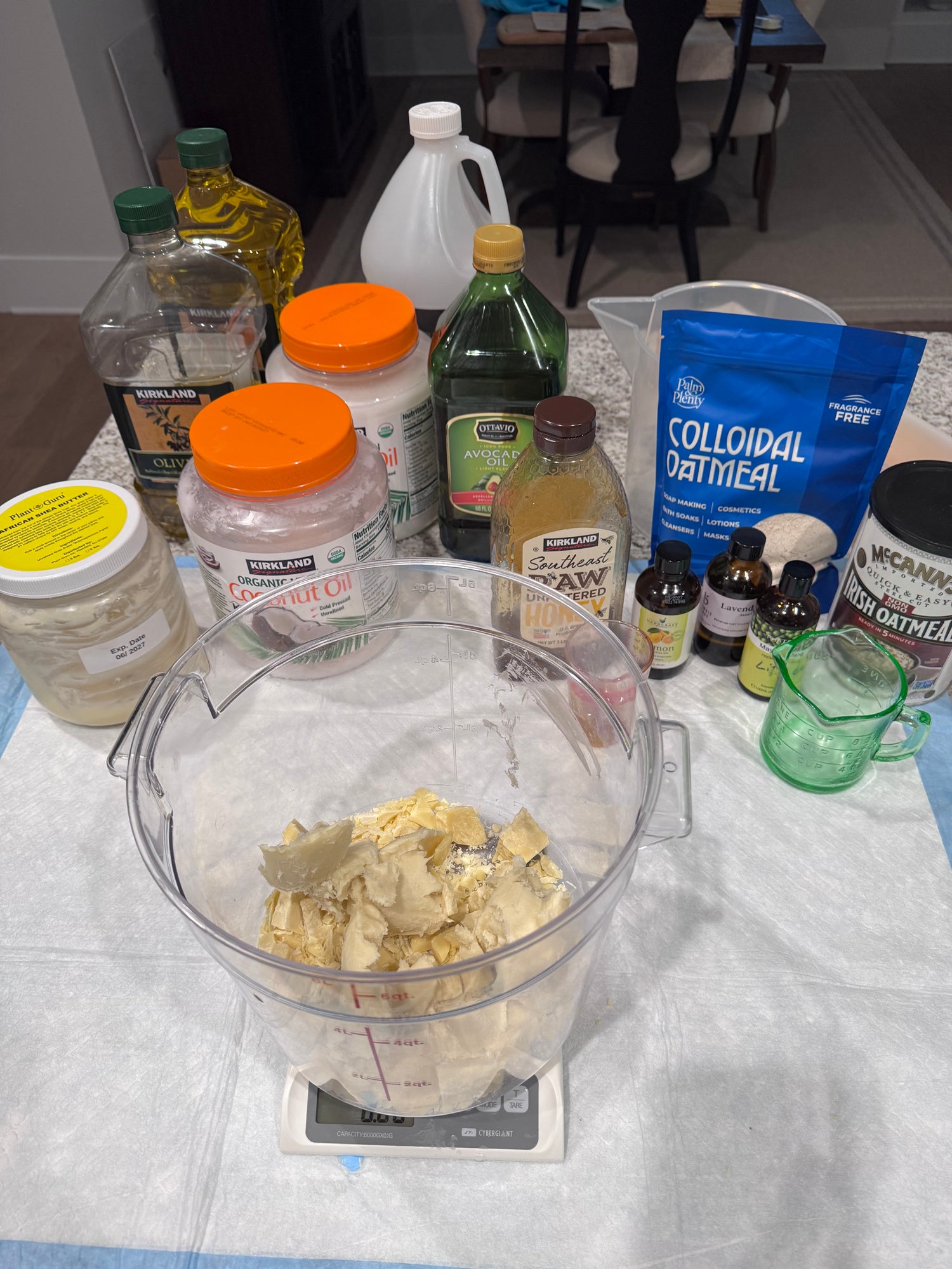 Tabletop scene with containers of oils and butters. Large container on a kitchen scale, honey, oatmeal, essential oils and measuring cup on a white surface.