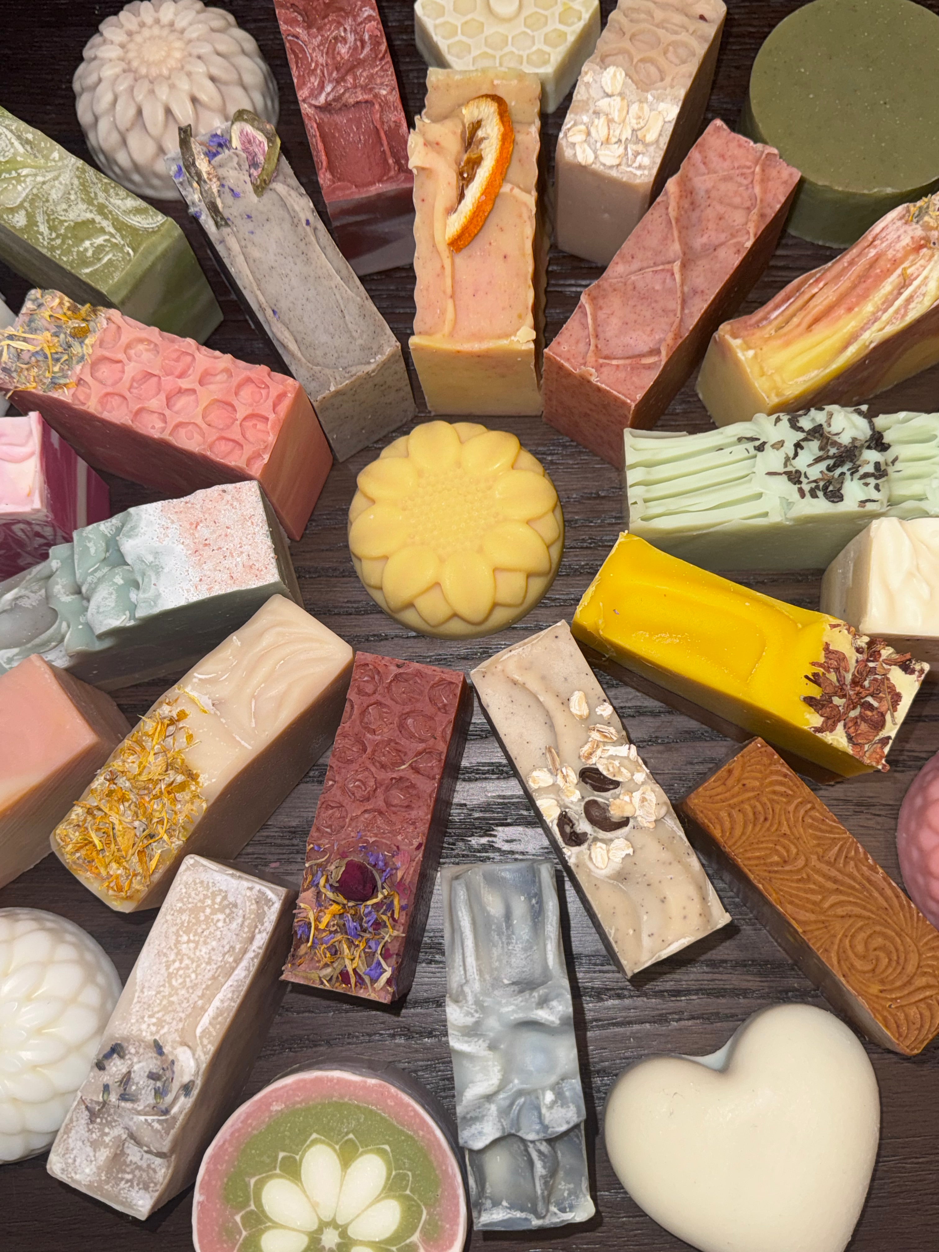 Assorted decorative soaps of various shapes, sizes, and designs on a dark surface.