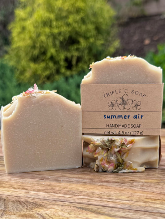 Handmade soap with packaging labeled 'Triple C Soap Summer Air' on a wooden surface with a blurred natural background.