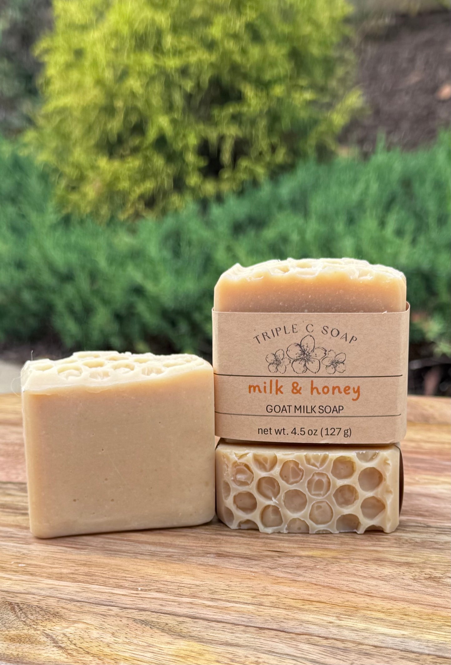 Three bars of milk & honey goat milk soap labeled 'Triple C Soap' on a wooden surface with a natural background.