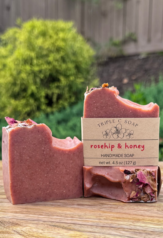 Handmade soap bars with 'Triple C Soap' rosehip & honey label on a wooden surface outdoors.