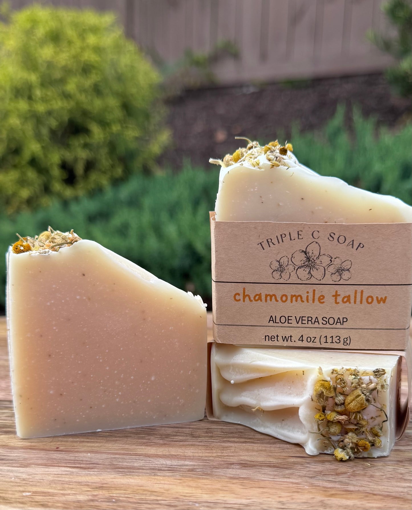 Three bars of chamomile tallow aloe vera soap with packaging on a wooden surface.