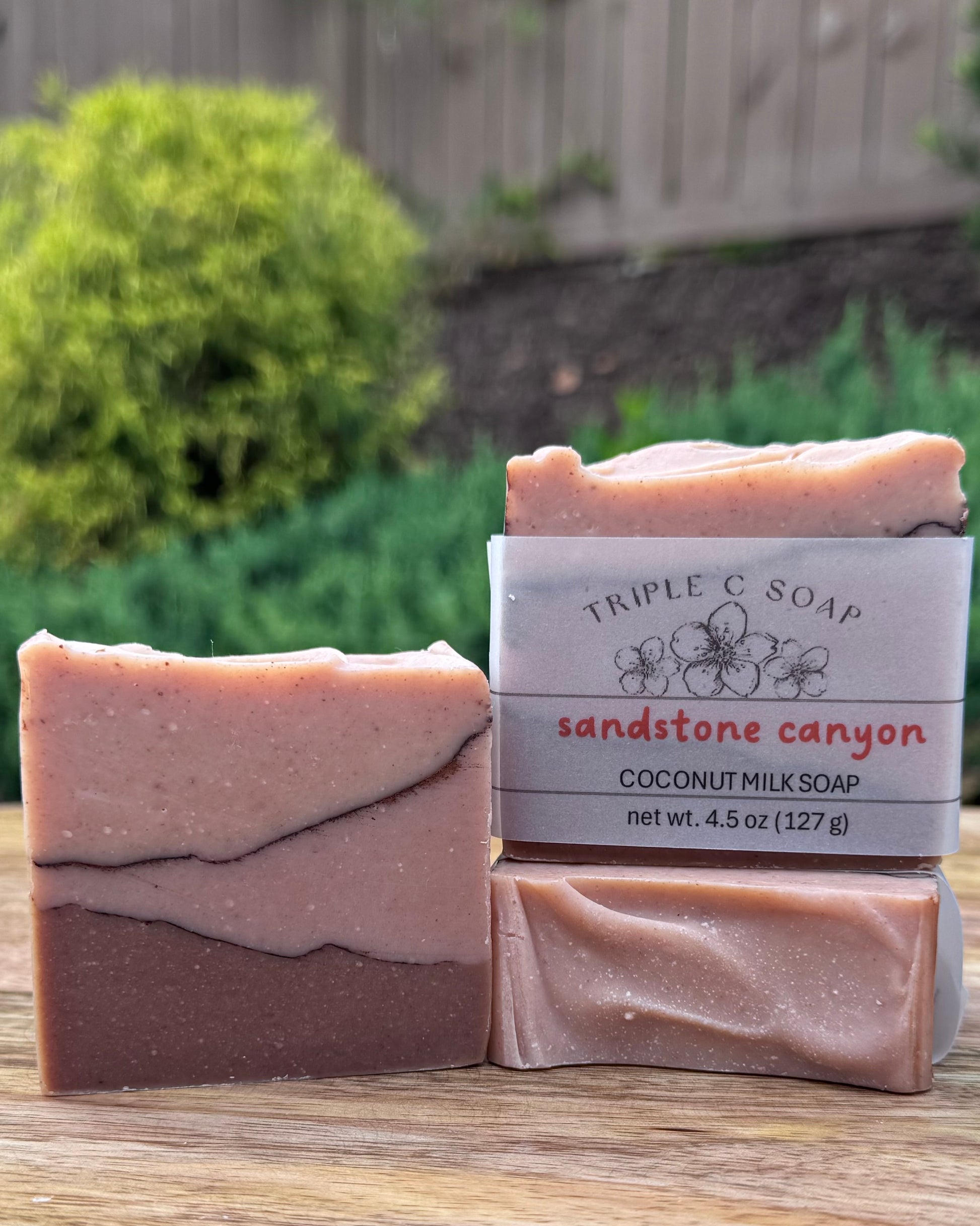 Three bars of soap labeled 'Triple C Soap Sandstone Canyon' on a wooden surface with a garden background.