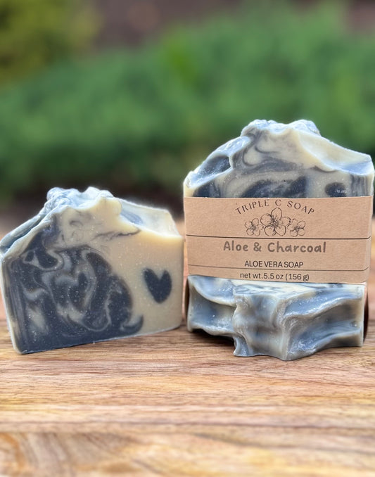 Three bars of aloe and charcoal soap with a label on a wooden surface.