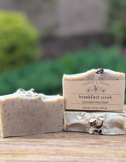 Three bars of Breakfast Scrub soap with a label on a wooden surface outdoors