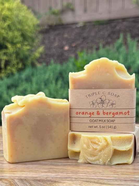 Three bars of soap labeled Orange & Bergamot on a wooden surface outside.