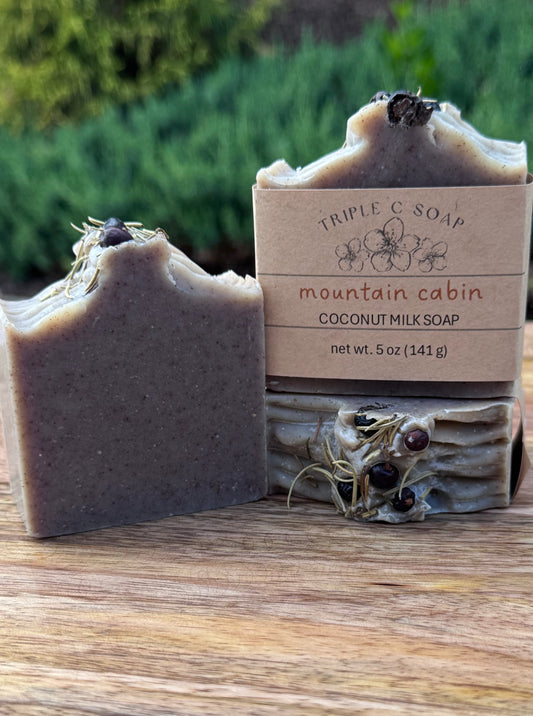 Three bars of soap labeled mountain cabin coconut milk soap on wooden surface outside.