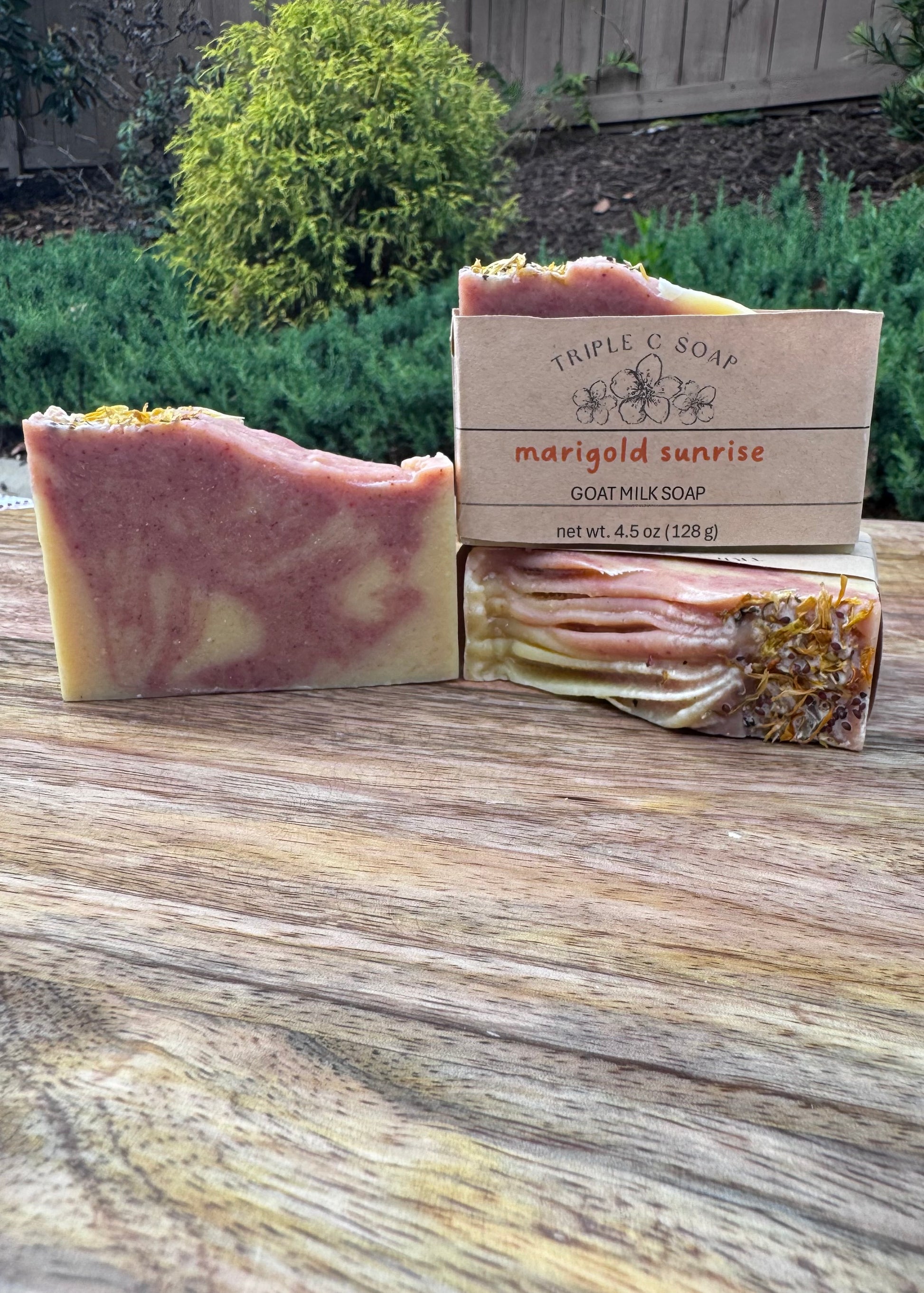 Three bars of soap with a labeled 'Triple C Soap' Marigold Sunrise on a wooden surface outdoors.