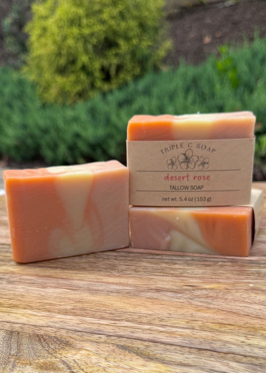 Three bars of soap labeled 'Triple C Soap' Desert Rose on a wooden surface with a blurred natural background.
