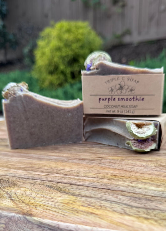 Three bars of soap labeled 'Purple Smoothie' sitting on a wooden surface in front of a natural background.
