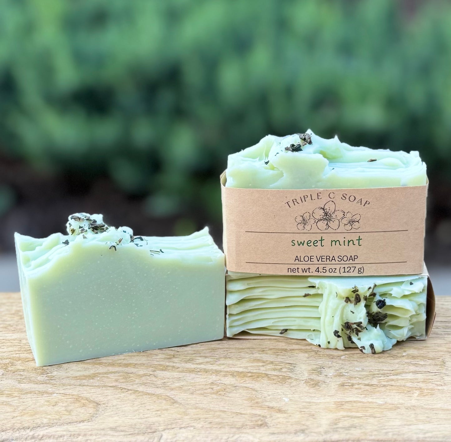 Three bars of sweet mint aloe vera soap on a wooden surface.
