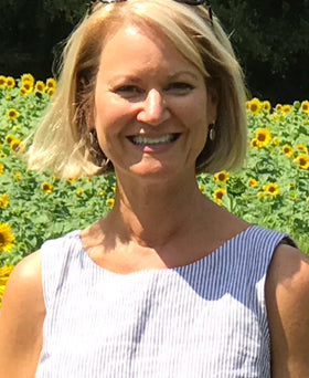 Woman standing in front of sunflowers wearing a sleeveless dress.